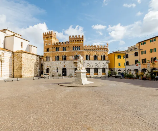 Sunny European square with historic buildings and central statue.