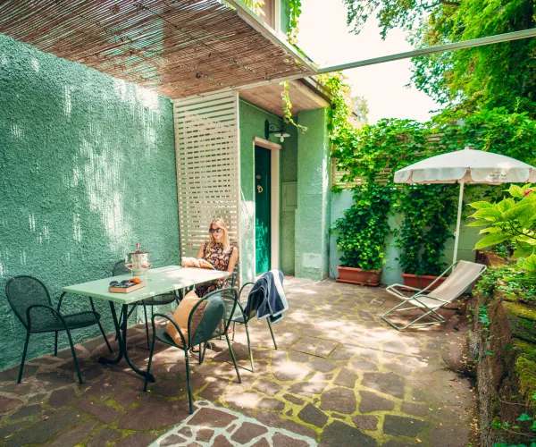 Cozy patio with green walls, a small table, chairs, and plants in sunlight.