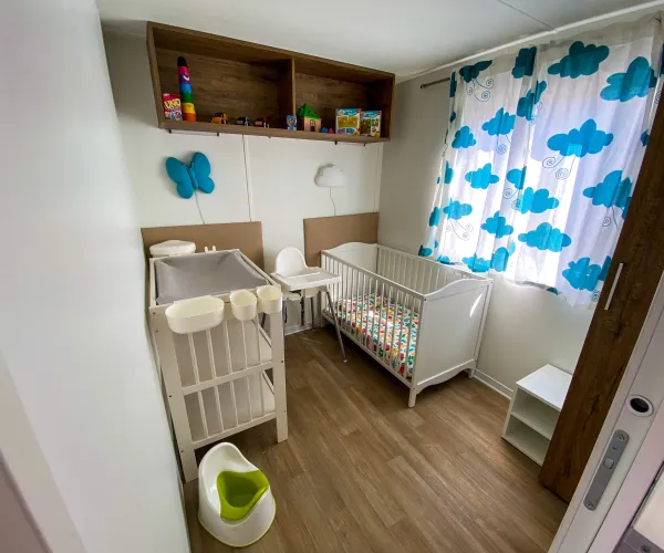 Compact nursery with crib, changing table, cloud-pattern curtains, and toys on shelves.
