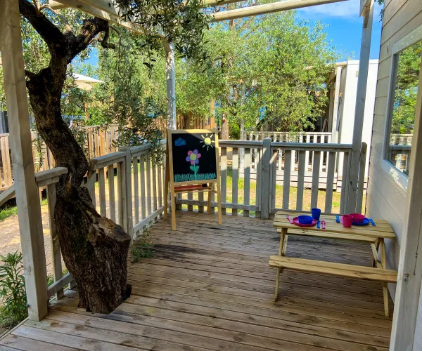 Wooden porch with playhouse, tree, chalkboard, and toy picnic table.