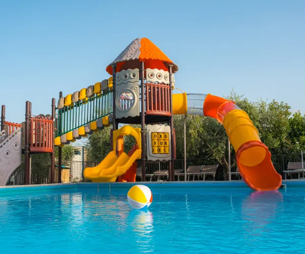 Colorful playground slide ending in a swimming pool, with a beach ball floating nearby.