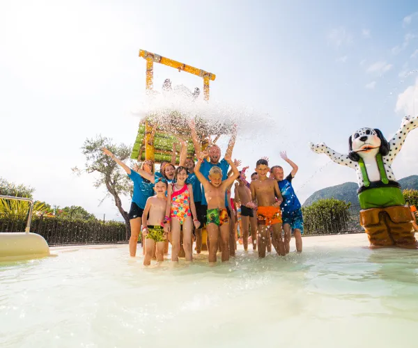 Children play in a water park splash area, joyful expressions, sunny day.