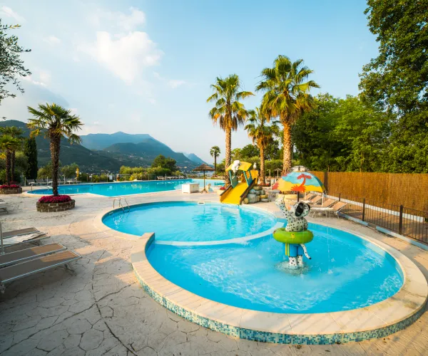 Outdoor pool with palm trees, mountains, and a water slide on a sunny day.
