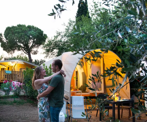 Couple embracing near illuminated tent in a garden setting.