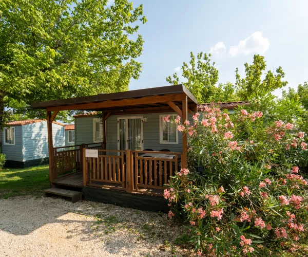 Cabin with a wooden porch, surrounded by trees and blooming pink flowers.