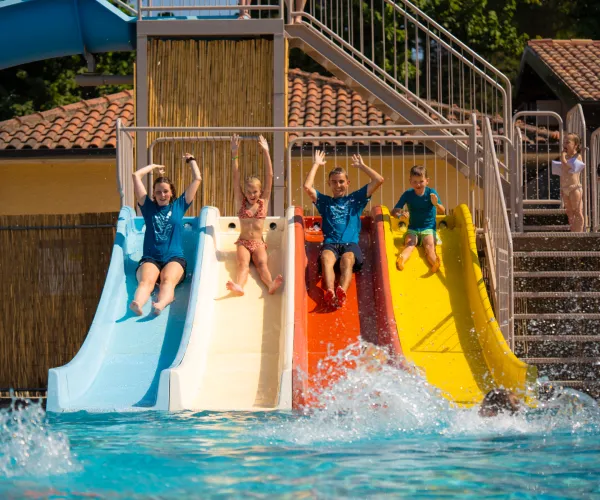 Kids sliding down colorful waterslides into a pool.