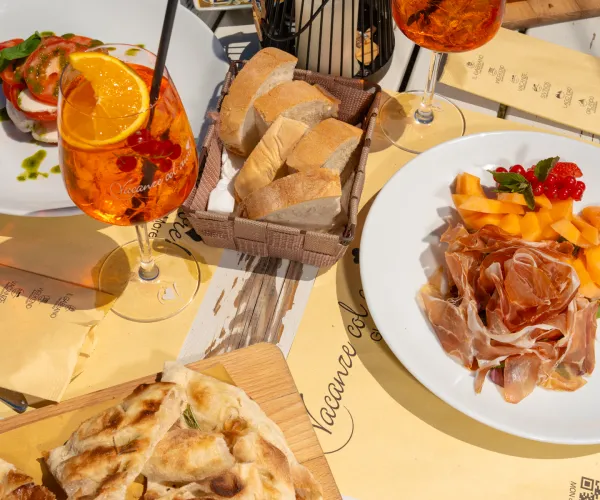 Italian meal with Aperol Spritz, bread, cured meat, and fruit on a sunlit table.