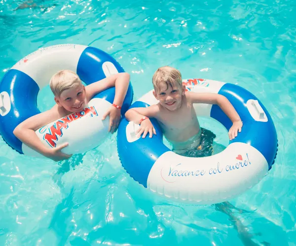 Two children smiling in pool with blue and white float rings.