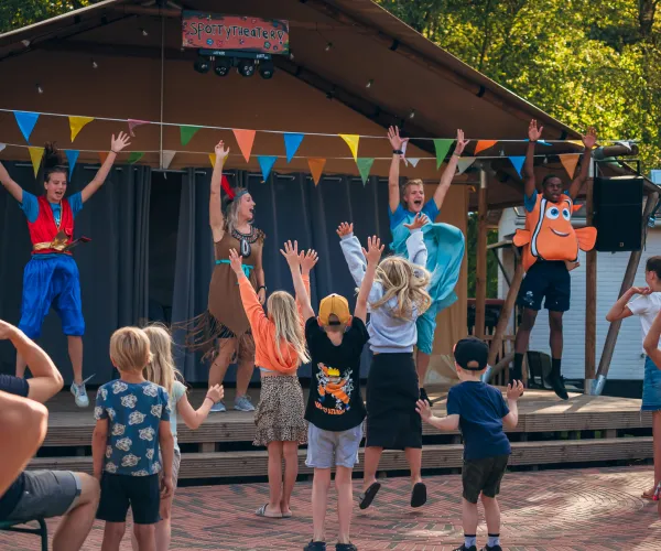 Children dancing in front of a stage with performers in costumes.