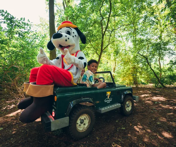 Costumed character and person in toy Jeep in a wooded area.
