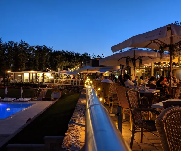 Outdoor restaurant at dusk, illuminated with string lights, near a pool.