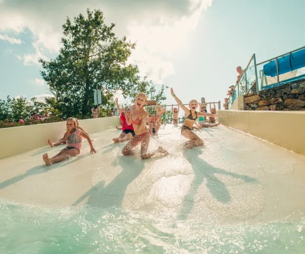 Children sliding down a water slide on a sunny day, splashing and smiling.