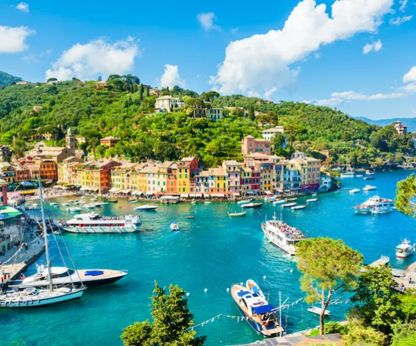 Colorful harbor town with boats, surrounded by green hills and blue sky.