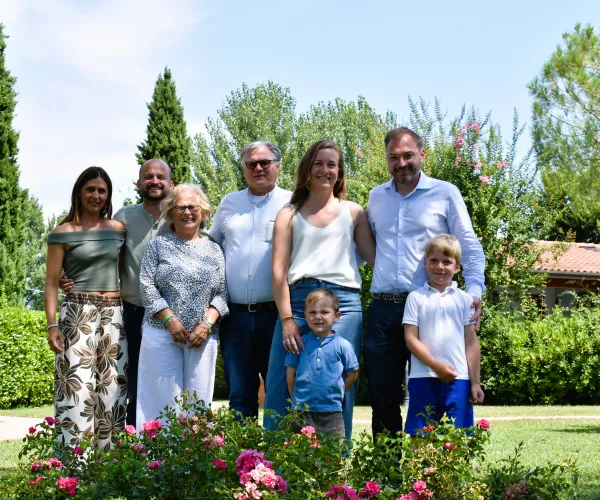 Family posing together in a garden with flowers and trees on a sunny day.