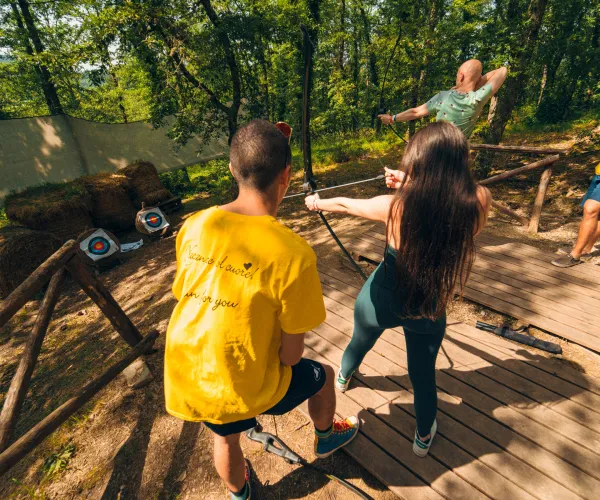 People practicing archery in a sunny forest setting.