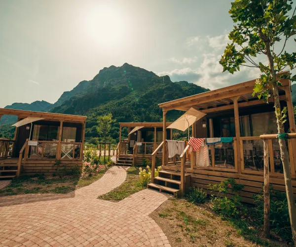 Cabins with porches under a bright sky, mountain backdrop.