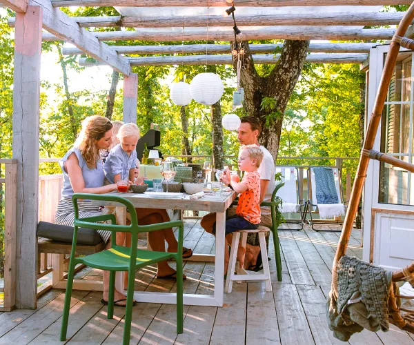 Family dining on a sunny patio surrounded by trees.