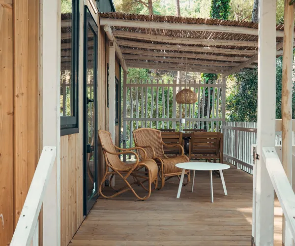 Cozy veranda with wicker chairs, sofa, and a white table under a pergola.