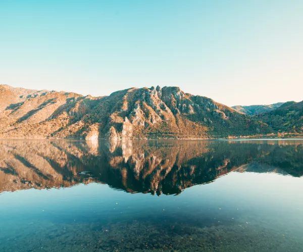 Calm lake reflecting mountains under clear blue sky.