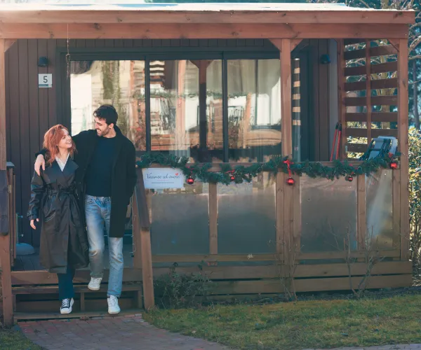 Couple smiling in front of a wooden cabin decorated with garlands.