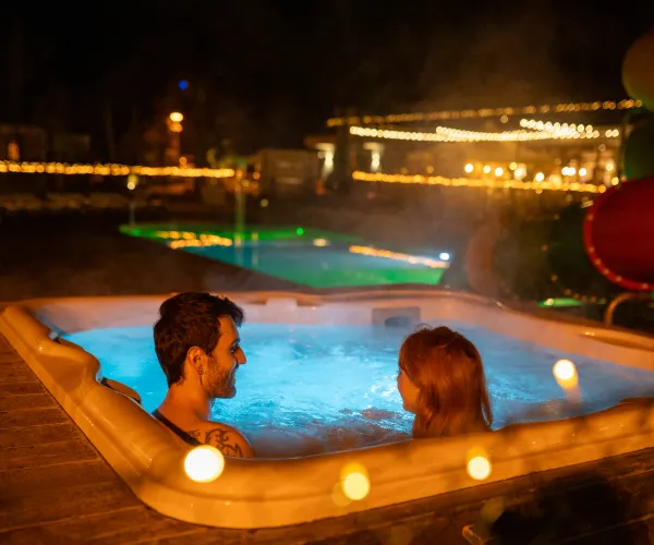Couple relaxing in a hot tub at night, surrounded by warm lights.