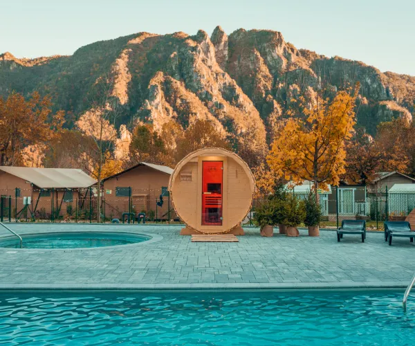 Mountain resort with pool, hot tub, and barrel sauna at sunset.