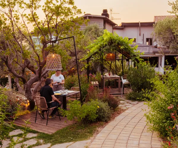 Garden dining scene at sunset with two people seated under trees.