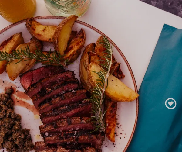 Steak and potatoes with garnish on a plate beside a teal napkin.