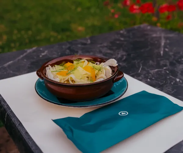 Salad in a brown bowl on a table with a blue napkin.