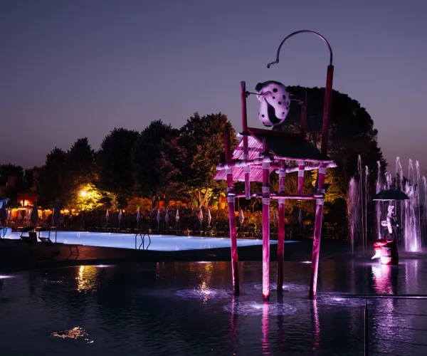 Nighttime sculpture with purple lights by a fountain, trees in the background.