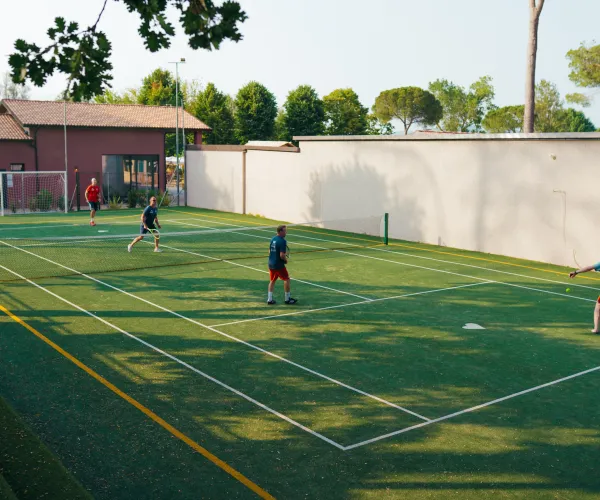 Two people playing padel on an outdoor court surrounded by trees.