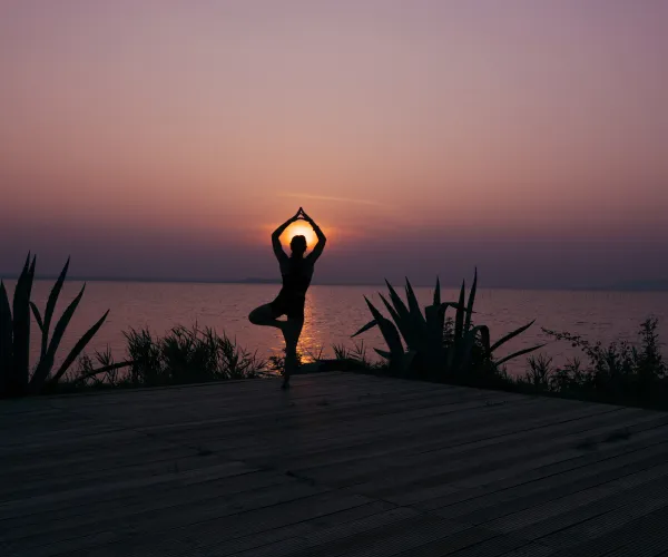 Yoga pose by a lake at sunset, silhouette against a purple sky.