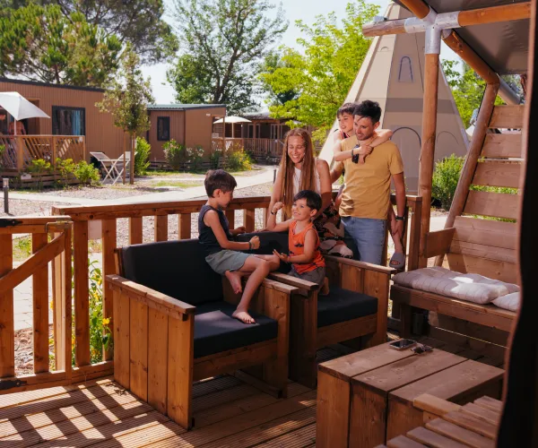 Family relaxing on a wooden porch with cabins in the background.