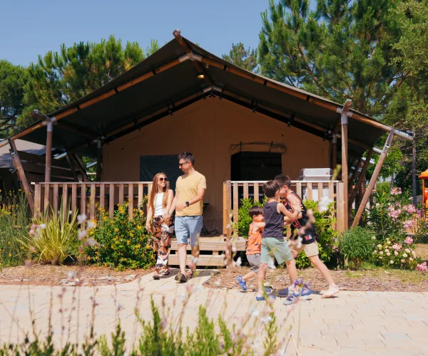 Family walking near a cabin with trees and flowers.