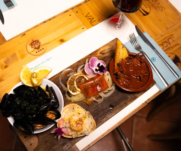 Seafood and meat platter on a wooden table, with wine nearby.
