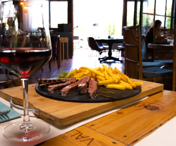 Steak and fries on a plate with a glass of red wine in a restaurant setting.