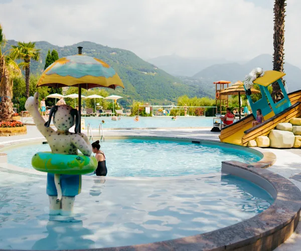 Water park with a statue holding an umbrella, mountains in the background.