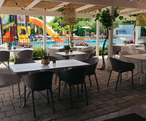 Outdoor café with tables and chairs by a pool, bright slide in background.