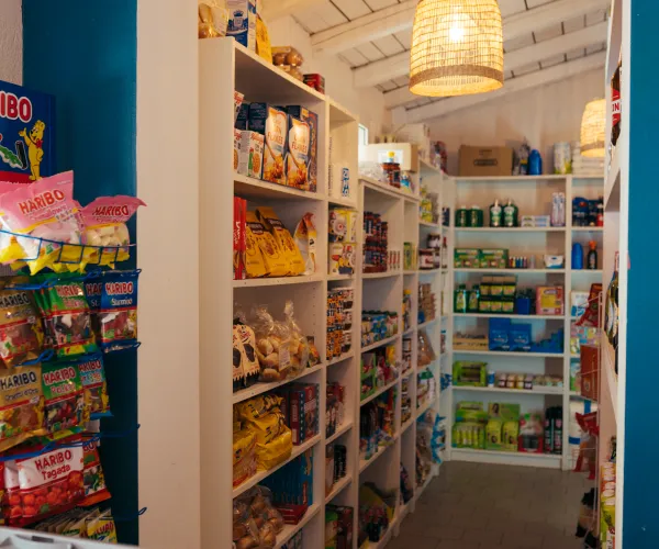 Small shop interior with shelves of snacks and groceries, bright lighting, and blue walls.