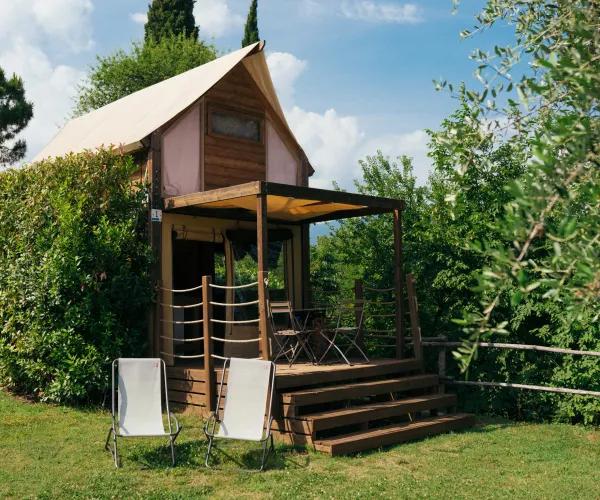 Rustic wooden cabin with a sloped roof, surrounded by greenery. Two chairs in front.
