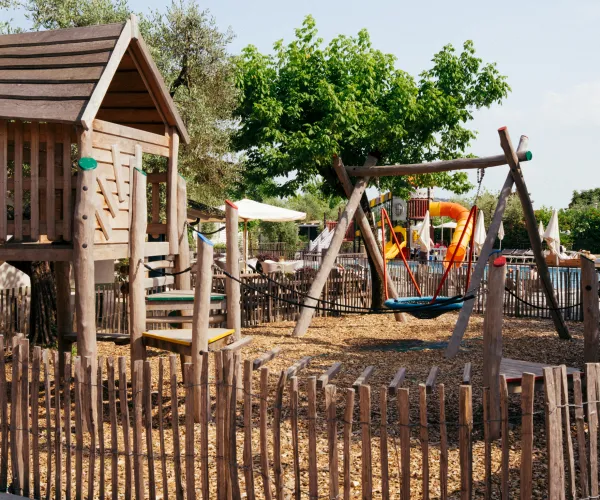 Wooden playground with slide and swings, surrounded by trees.