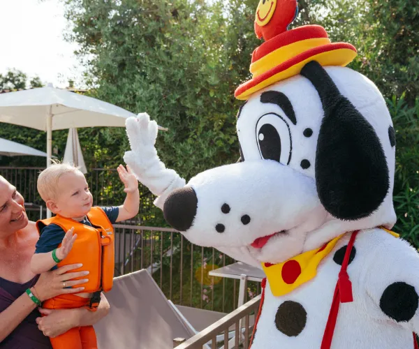 Child and woman greeting a large dog mascot in a playful setting.