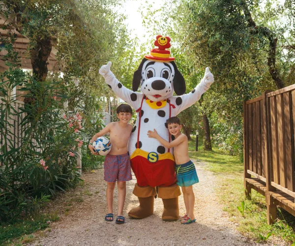 Dalmation mascot with two smiling children outdoors, one holding a soccer ball.