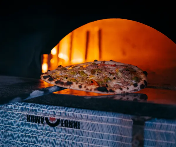 Pizza baking in a wood-fired oven, flames glowing orange.