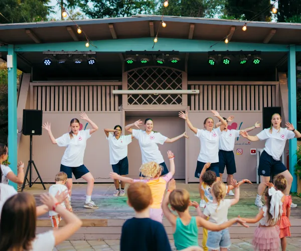 Group of performers dancing on stage, children watching and joining in.