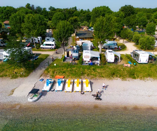 Campsite by a lake with boats, RVs, and tents, surrounded by trees.