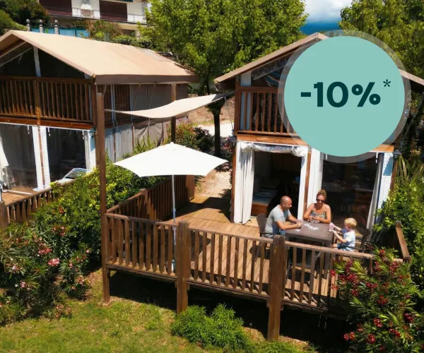 Two wooden cabins with verandas, people dining outside, surrounded by greenery.