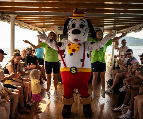 Mascot dog dances on a boat with cheering passengers around.