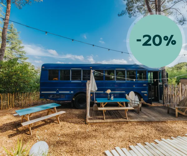 Blue bus on a sunny campsite with picnic tables under string lights.
