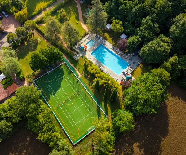 Tennis court and pool surrounded by lush greenery, aerial view.